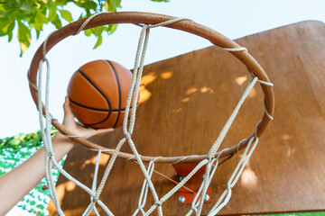 Fototapeta na wymiar close view of hands throwing a ball into a basketball basket, teenage boy playing at home in the backyard, outdoor activities on summer vacation