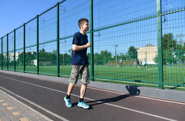 a teenage boy trains on a sports ground outdoors, he runs, does physical exercises, a healthy lifestyle, a bright sunny day in summer