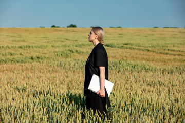 employee of an agricultural firm with a laptop checks the quality of wheat in the field