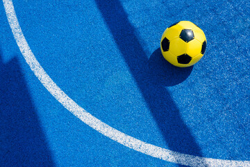 Colorful sports court background. Top view light blue field rubber ground with white line , shadow from football goal net and yellow soccer ball on sunny day outdoors