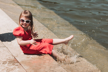 Beautiful little girl in red dress and with glasses playing outdoor with water