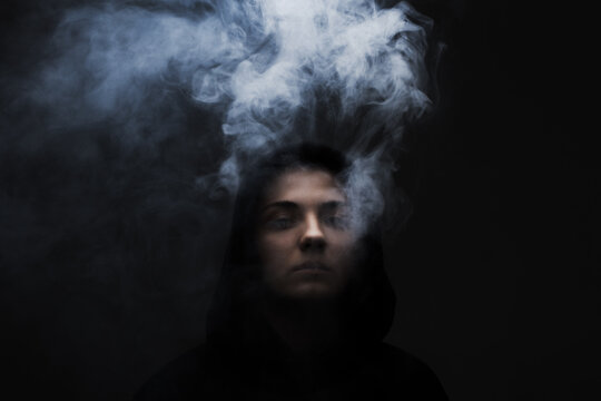 Dark portrait of a short haired girl wearing hoodie with smoke coming out of it. .