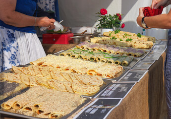 A market stall with sweet and savoury potato pancakes called lokse. A customer buys food at a stall selling potato pancakes. Focus on the pancakes with grated cheese and the customer with his wallet.