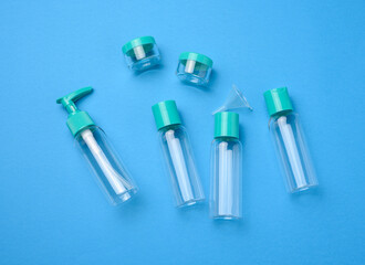 Various transparent empty plastic bottles and jars for cosmetics on a blue background, top view