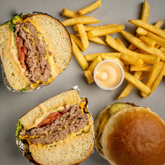 table with double cheeseburger and hamburger cut in half, french fries and sauce top view