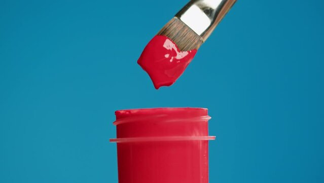 Red paint isolated on blue background. Bright gouache falling from paintbrush close-up. Drawing hobby and art concept.