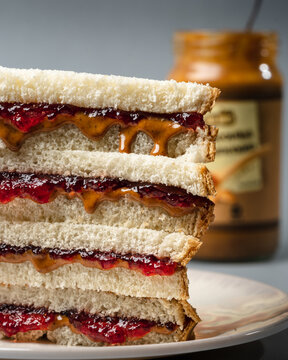 stack of peanut butter and strawberry jelly sandwich and jar of peanut butter out of focus in background