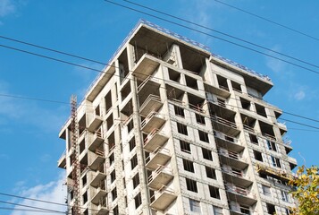 A high quality photo of straight multi-storey buildings and lines of electrical constructions situated in the city on of a blue sky with no clouds as a background. Construction of a residential area.