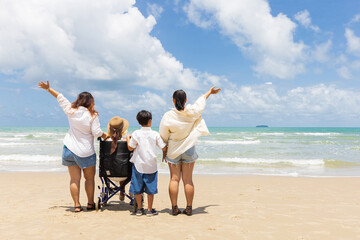 back view woman in a wheelchair with family and looking to sea on the beach