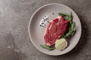 Raw beef steak with rosemary, garlic, salt, and pepper.