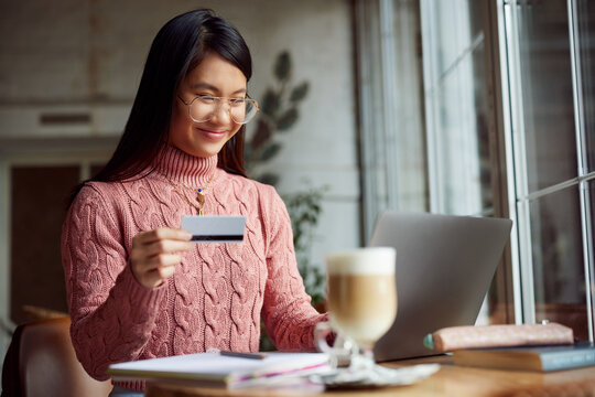 A happy Asian girl is using credit card for online purchase on the laptop.