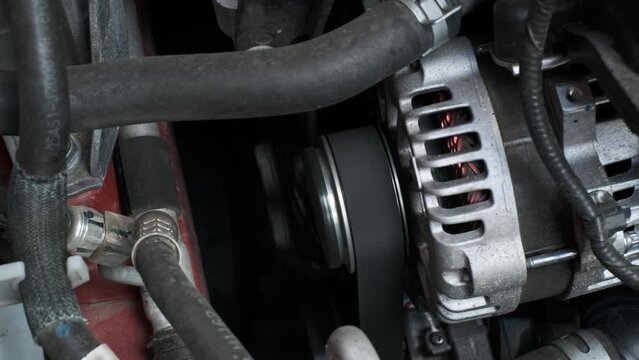 close view of car's generator which is spinning and giving voltage to entire onboard network of vehicle. Gasoline or diesel car with running engine. Close view of internal parts of engine.