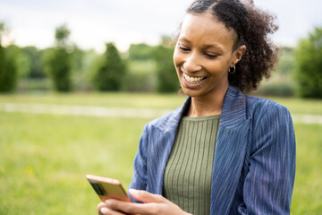 Young caribbean woman reading a message of his best friend and smile while enjoying a good day outdoor.