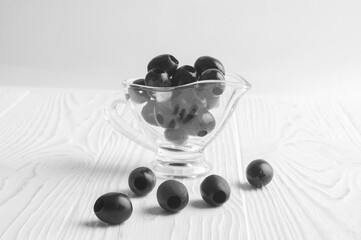 black olives lie in a transparent cup on a white wooden background
