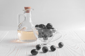 olive oil in a jug and black olives lie in a transparent cup on a white wooden background