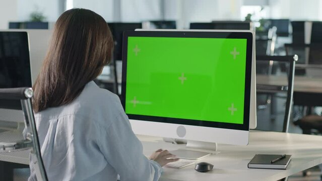 Over The Shoulder Shot Of a Business Woman Working In Office Interior On Pc On Desk, Looking At Display Green Screen. Office Person Using Computer With Computer Green Screen, Sitting at Table.