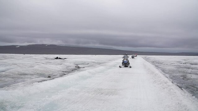 Group of tourists riding snowmobiles with a guide at Vatnajokull glacier in Iceland. Active sport, recreation, lifestyle.