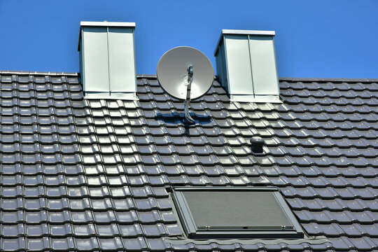 Satelliten-Antenne, Metall-Schornstein und Dachfenster auf einem Ziegeldach