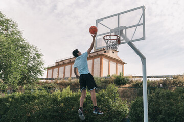 Young basketball player making a drop shot in the heights. Sporty dark-haired man holding onto the rim of the basket after scoring a great point in a street basketball game. Sport concept.