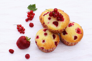 Summer baking - delicious homemade muffins with red berries - strawberries, raspberries and red currant. Baked muffins ready to eat, fresh fruits around