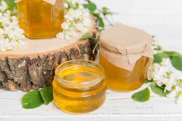 Sweet honey jar surrounded spring acacia blossoms. Honey flows from a spoon in a jar. jars of clear fresh acacia honey on wooden background