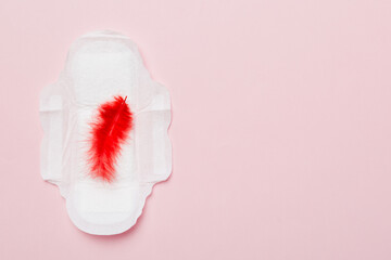 Women hygiene products or Sanitary pad with red feather on colored background. Pastel color. Closeup. Empty place for text. Female daily hygiene © sosiukin