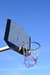 Basketball hoop and net against a blue sky. Urban youth game. Low angkle view below the hoop net. Concept of success and scoring.