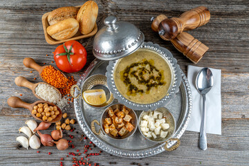 Soup in copper cup on wooden table, onion, spoon,lentil ,rice,chickpeas,garlic etc all ingredients around, Traditional soup Turkish name Mahluta.