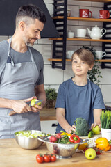 Handsome father and his teenager son spending quality time together. Men doing chores, cooking healthy vegetable salad, tasty food in the kitchen at home
