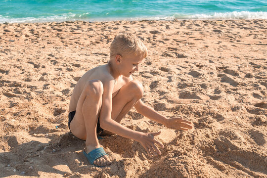 A boy on a sandy sea beach enthusiastically plays with sand. Happy summer vacation at sea