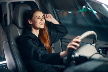 a happy, relaxed woman enjoys a night drive while sitting in a car and holding her hand near her head in a relaxed pose
