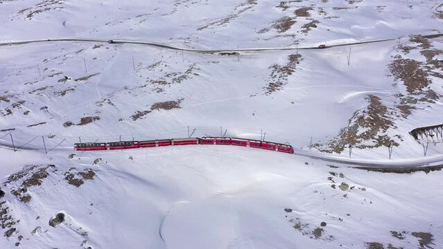 Bernina Express Train in Switzerland near Bernina Pass on Sunny Winter Day. Bernina Railway. Swiss Alps. Aerial View. Drone Flies Sideways