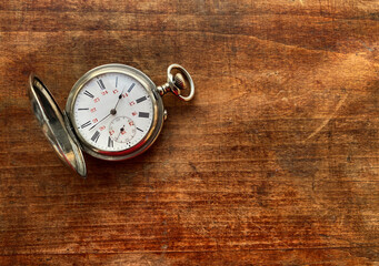 An old pocket watch with Roman numerals on a wooden table in vintage style. The passing time.