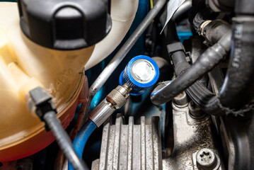 A blue quick-release coupler is installed on the valve from the air conditioning system in the car...