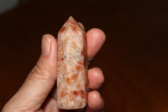 Person holding a polished sunstone point also known as a sunstone tower crystal. Sunstone is a healing stone that works across the physical, spiritual, and emotional plains. (heliolite) gem stone