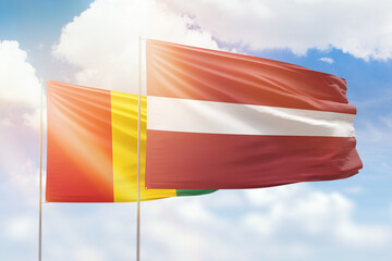 Sunny blue sky and flags of latvia and guinea