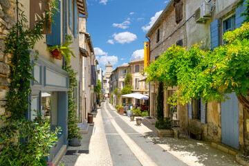 Fototapeta na wymiar A picturesque street through the historic town of Saint-Remy de Provence, France, with the colorful shops and cafes and the clock tower in view on a summer day.