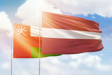 Sunny blue sky and flags of latvia and oman