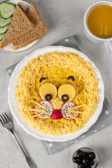 Fun food for kids breakfast - cute lion head made from scrambled eggs, cheese, radishes and black olives on white plate, Top view