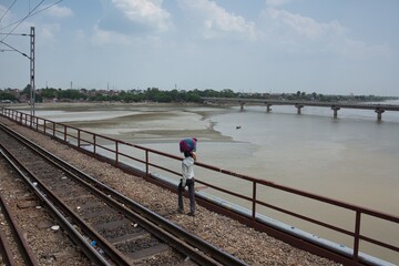 A man walks along the railroad tracks with a package on his head. India.