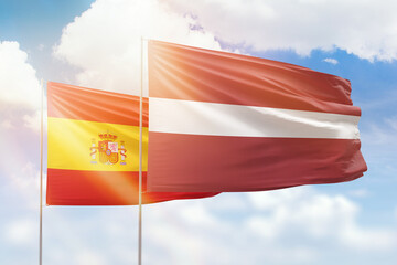 Sunny blue sky and flags of latvia and spain