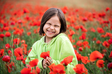 Portrait of little girl smiling and standing against poppies field in summer