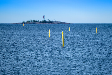 A line of yellow navigational buoys floating on the water. A small island in a background.