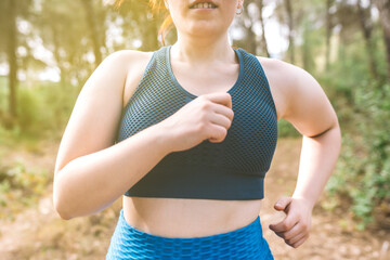 Fototapeta premium cropped shot young woman running through a forest on a summer day. female athlete doing sport outdoors. wellness and healthy living concept.