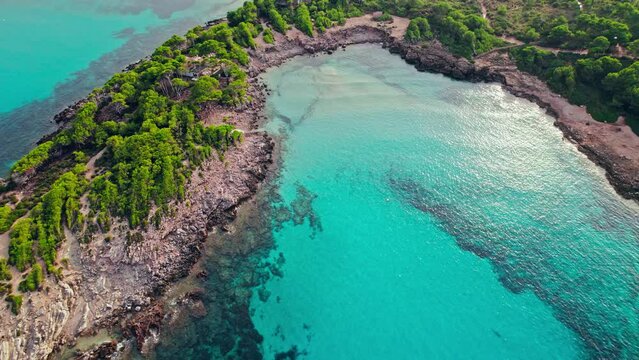 Vessel sailing by a Beautiful tropical green rocky coast with turquoise waters. Paradise alike bay in Cala Agulla, Mallorca, Balearic Islands, Spain with a tourist boat exploring the location.