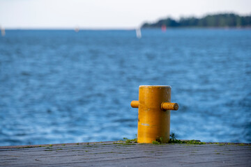 Naklejka premium Closeup of a mooring bollard against a bright blue sea. A small island in the horizon.