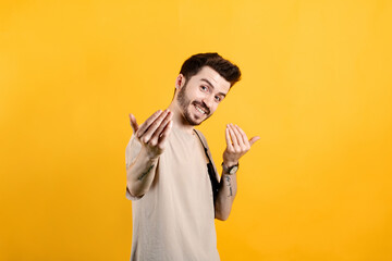 Handsome young man wearing casual clothes posing isolated over yellow background inviting to come closer with hands. Happy that you came. - obrazy, fototapety, plakaty