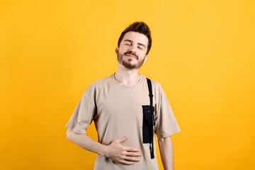 Young man wearing beige t-shirt posing isolated over yellow background hand on his stomach after...