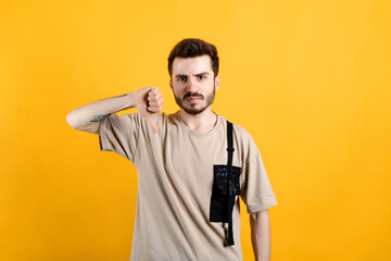 Caucasian young man wearing t-shirt posing isolated over yellow background showing thumb down and expressing dislike. Grumpy, dissatisfied, annoyed, unhappy.