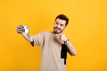 Handsome young man wearing casual clothes posing isolated over yellow background doing okay gesture while taking selfie or having video call.